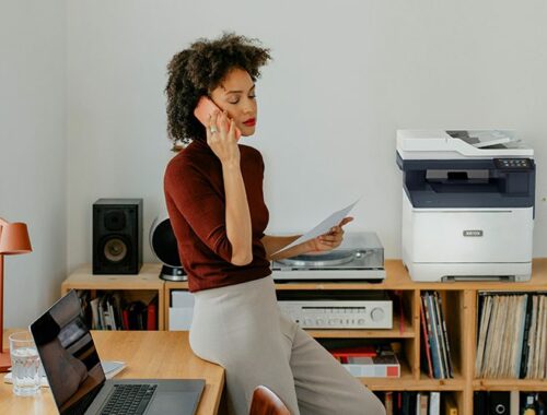 Une femme assise à un bureau en train de passer un appel à côté d'une imprimante Xerox® C325