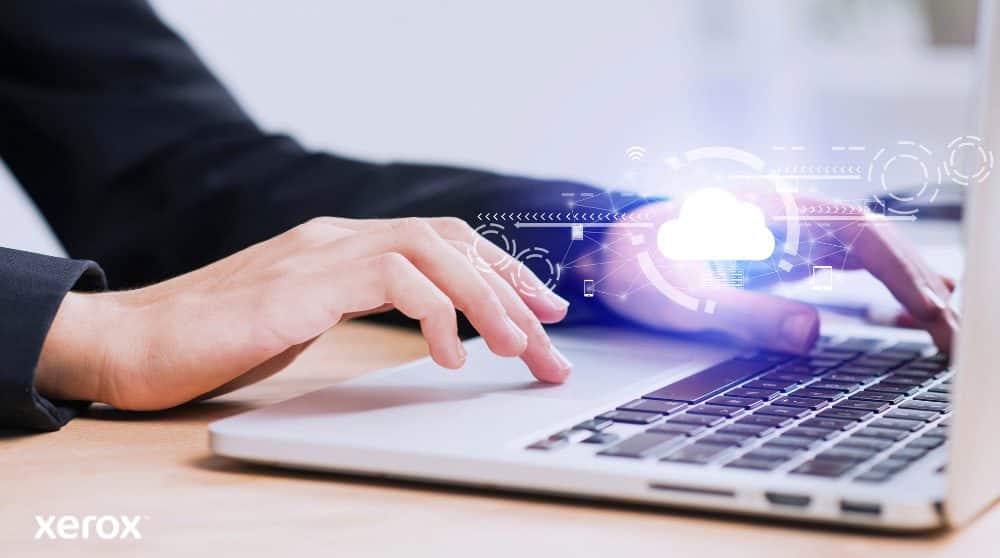 Les mains d'une personne sont représentées en train de taper sur un clavier d'ordinateur portable, avec une icône de nuage lumineux et des connexions réseau superposées sur l'image, symbolisant la connectivité cloud et les flux de travail numériques.