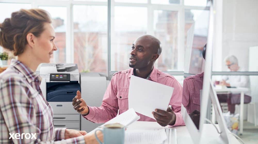 Une personne examine des données sur l'écran d'un ordinateur portable, avec une superposition numérique de diverses icônes d'appareils (imprimantes, appareils mobiles) et de lignes connectées, symbolisant la gestion centralisée de la flotte pour Xerox Workplace Solutions.